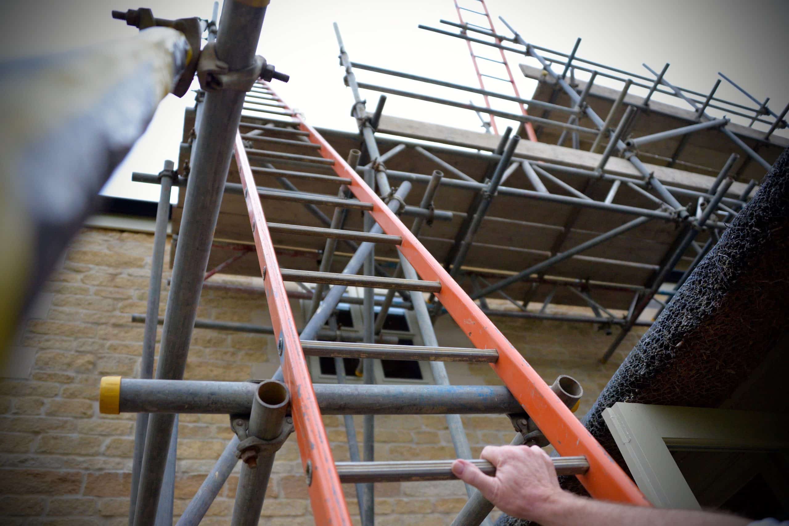 man climbing up a ladder to access scaffolding